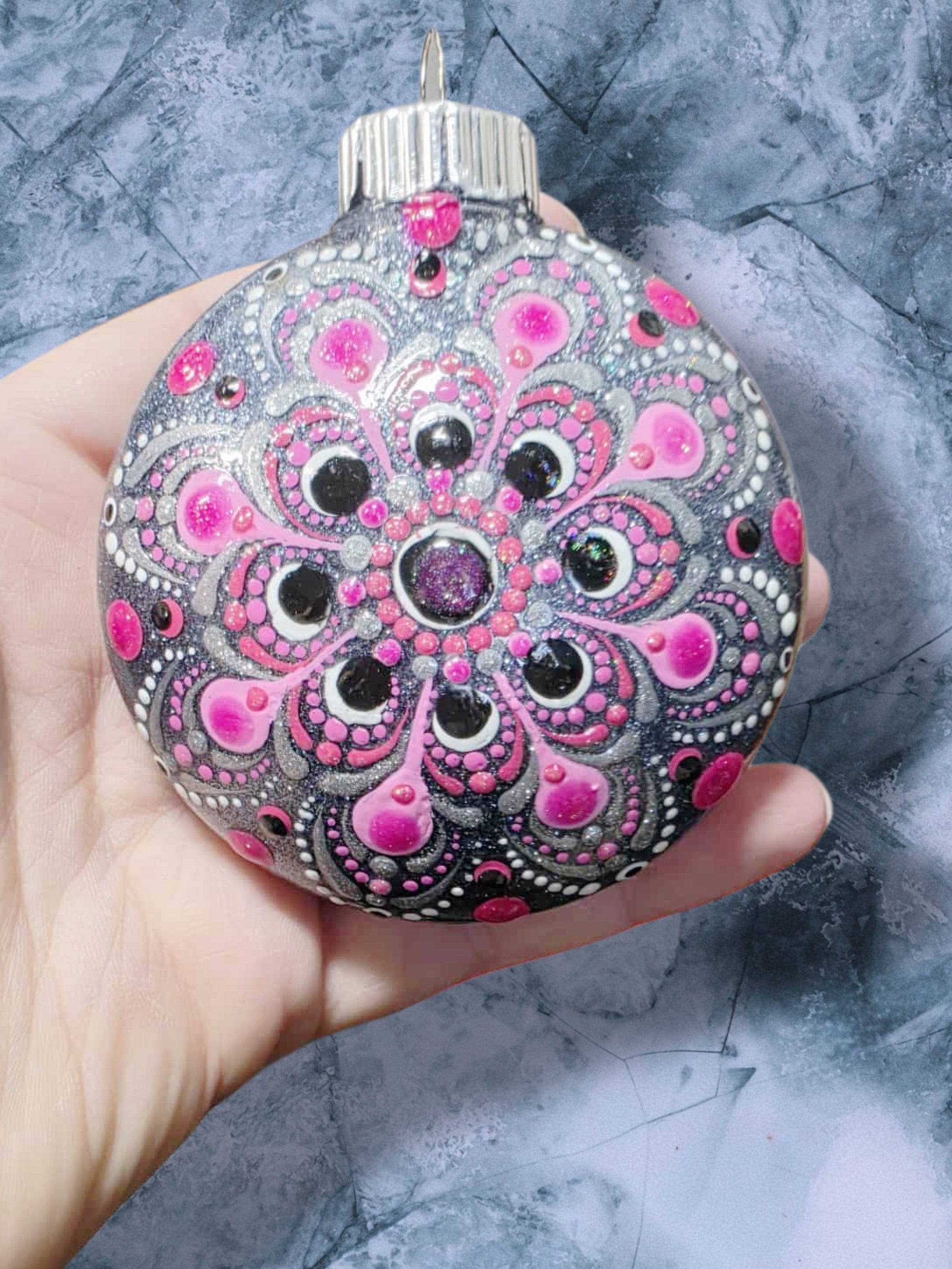 Christmas ornament decorated with a silver glitter base and a pink, black, and white mandala pattern.